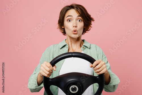 Young shocked surprised woman 20s wear green shirt white t-shirt hold steering wheel driving car look camera isolated on plain pastel light pink background studio portrait People lifestyle concept