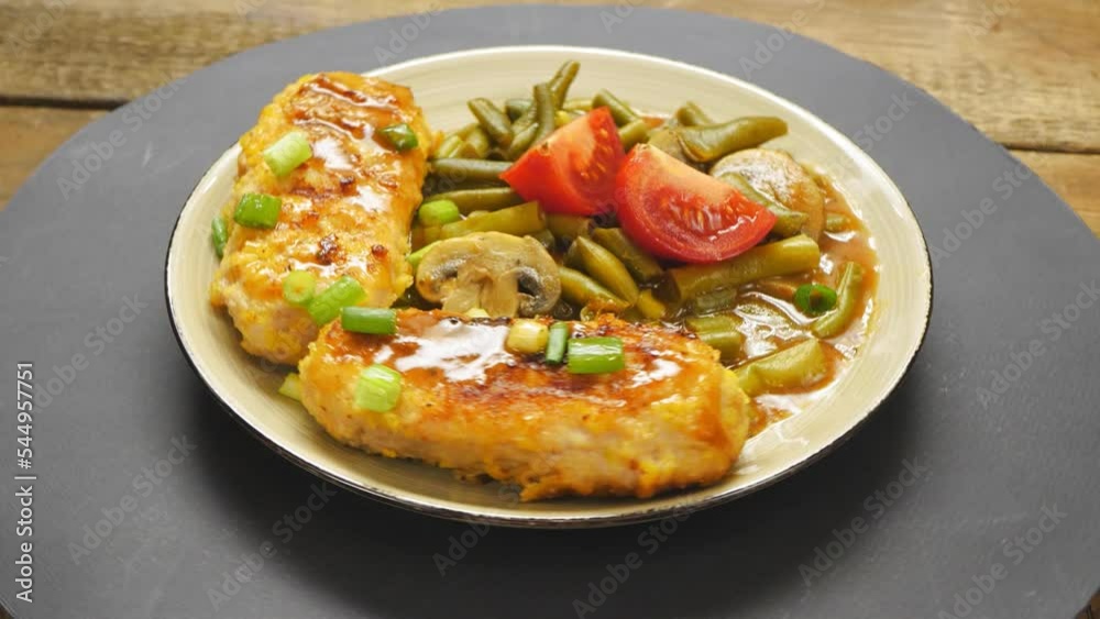 Cutlets with green beans and mushrooms in tomato sauce garnished with tomatoes and green onions in a plate rotate in a circle. Medium plan Cutlets with green beans and mushrooms in tomato sauce garnished with tomatoes and green onions in a plate rotate in a circle. Medium plan