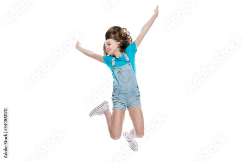 A teenage girl is jumping. A child in denim overalls and a blue T-shirt. Activity, joy and positive. Isolated on white background.