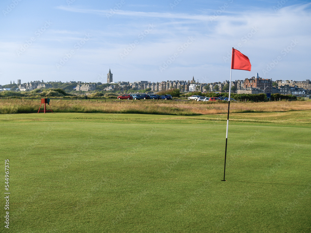 Obraz premium Red hole flag on golf course with urban skyline behind