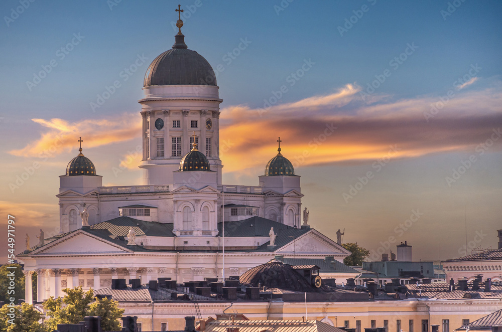 Helsinki, Finland - July 19, 2022: Closeup of golden sunset over the white stone Cathedral with cityscape up front under yellow-gray cloudscape