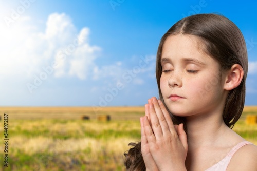 Happy young child praying on big field background.