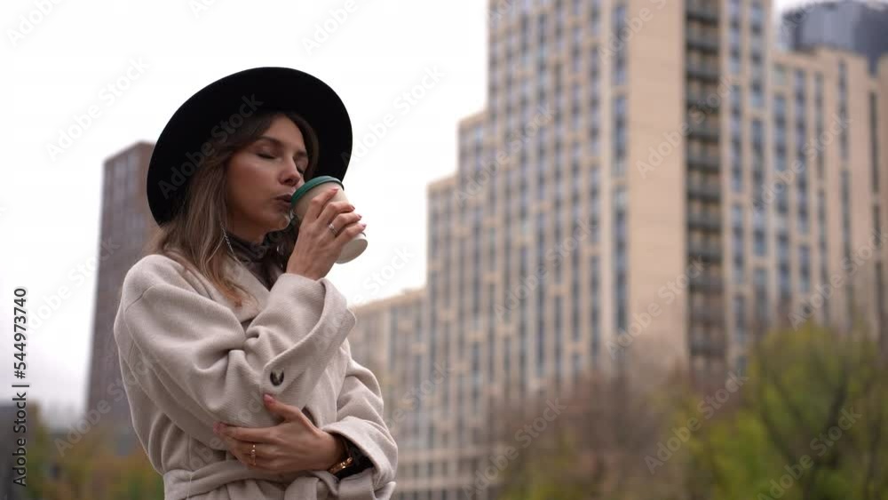 Girl in a hat on the background of skyscrapers drinks coffee in a cup
