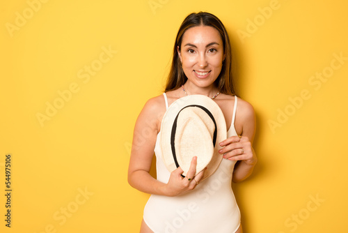 Happy young sexy woman slim body wear one-piece swimsuit straw hat posing isolated on vivid yellow color wall background studio. Summer hotel pool sea rest sun tan concept