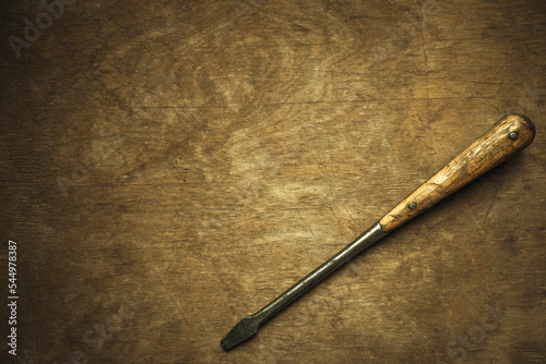 Antique screwdriver on a wooden background, a clean place for text. Vintage instrument. A huge screwdriver with wooden pads on the handle.