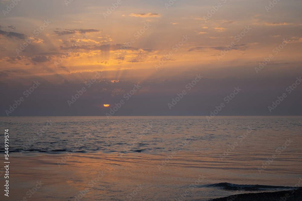 Sunset over the Black Sea. The rays of the sun break through the clouds. Warm spring evening on the beach in city of Sochi.