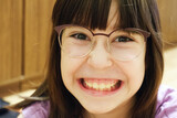 Little girl in glasses shows teeth grin