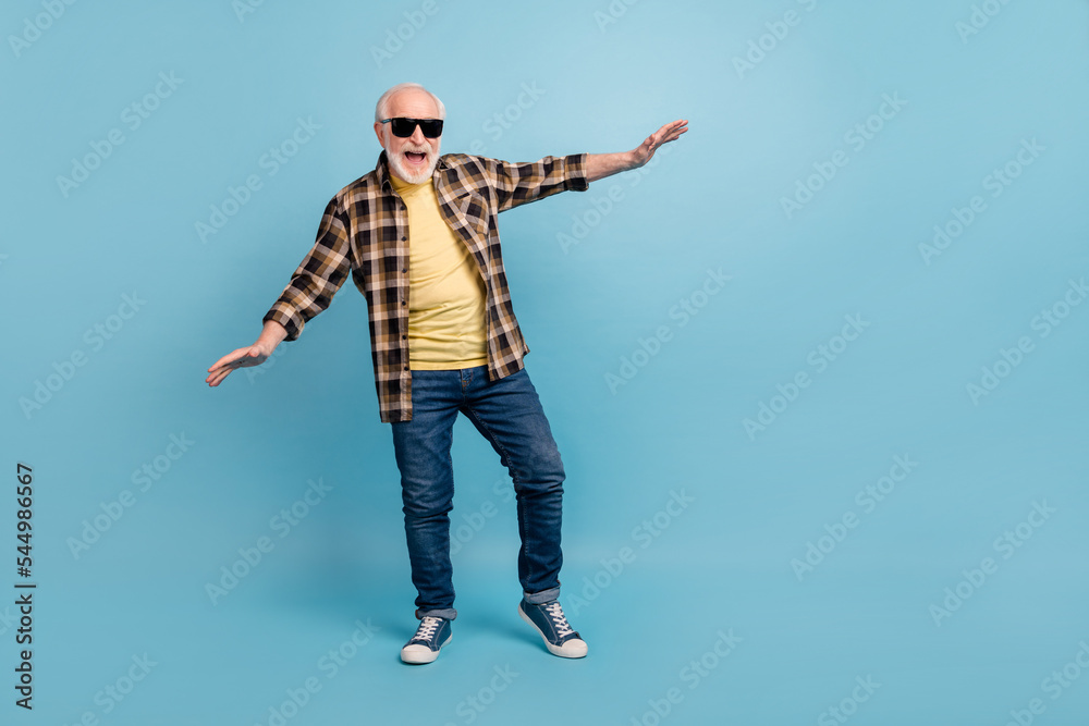 Photo of pretty funky retired man wear plaid shirt dark glasses dancing isolated blue color background Photo of pretty funky retired man wear plaid shirt dark glasses dancing isolated blue color background