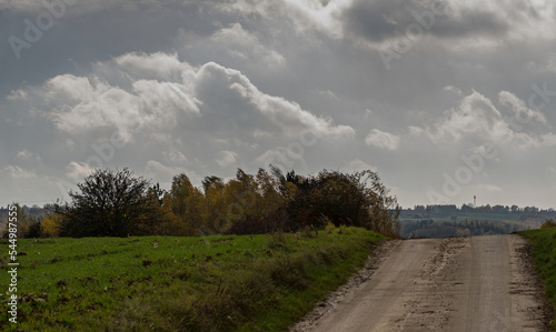 Asfaltowa droga biegnąca poprzez pola i wzgórza województwa Świętokrzyskiego . W tle dramatycznie zachmurzone niebo . 
