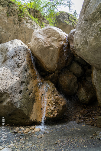 Small stream flows down from huge stones in a mountain gorge onto pebbles
