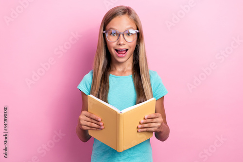 Photo of clever excited small kid wear turquoise t-shirt spectacles reading planner isolated pink color background