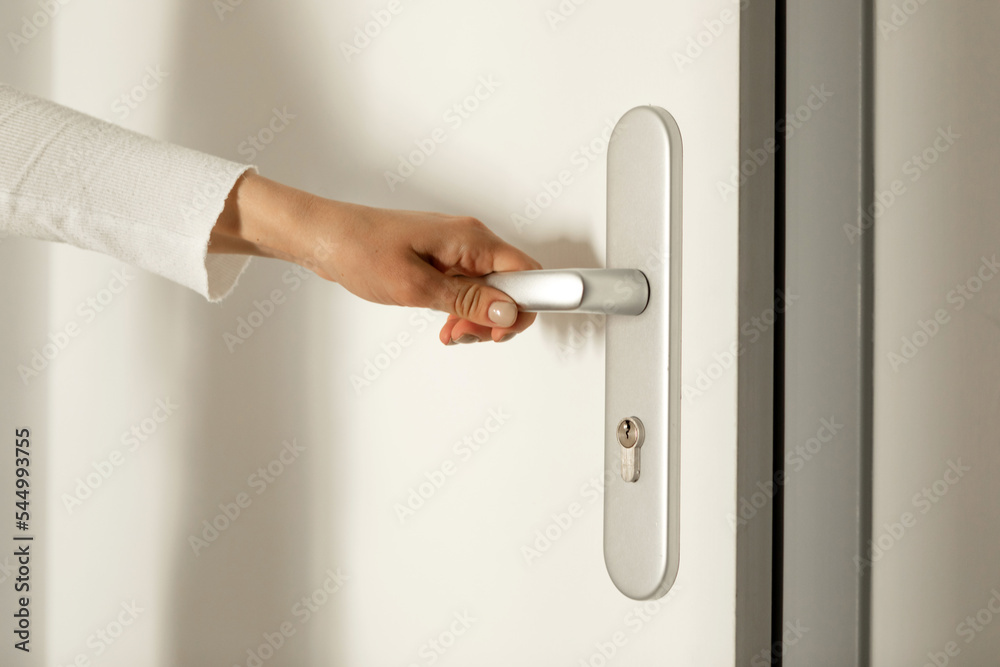 Hand opens the handle of a white wooden door Hand opens the handle of a white wooden door