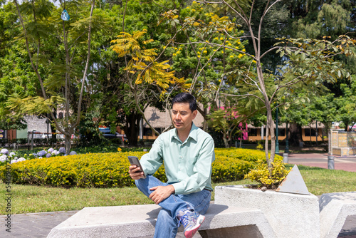 Latin man texting using cellphone in a park in guatemala city