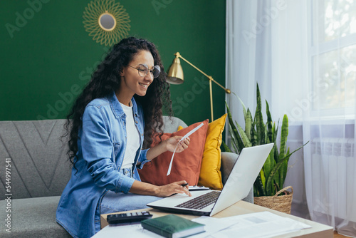 Quadro em tela Happy hispanic woman at home doing paperwork business woman calculating family budget and paying bills sitting on sofa in living room using laptop and calculator