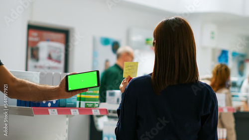 Smartphone showing horizontal greenscreen template in pharmaceutical shop, isolated display with chroma key on mobile phone. Blank mockup copyspace background on telephone in pharmacy.