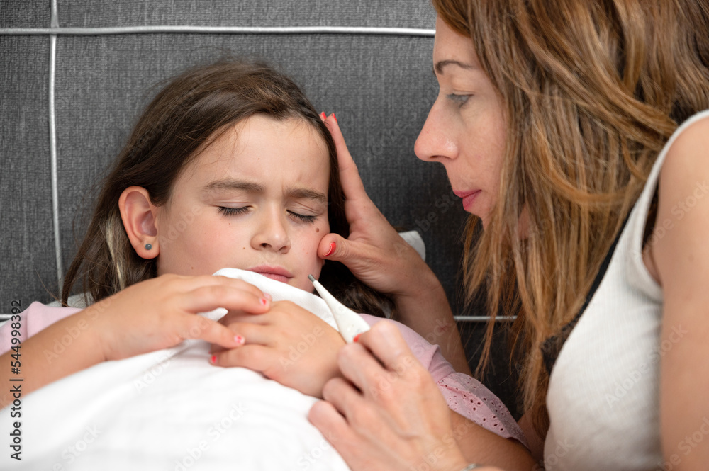 Mother measuring temperature of her ill daughter. Sick child with high fever laying in bed and mother holding thermometer. High quality photo Mother measuring temperature of her ill daughter. Sick child with high fever laying in bed and mother holding thermometer. High quality photo