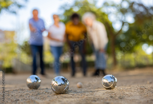 Mature casual diverse pensioners throwing petanque balls on the sand cover far away on a spring sunny day in the park photo