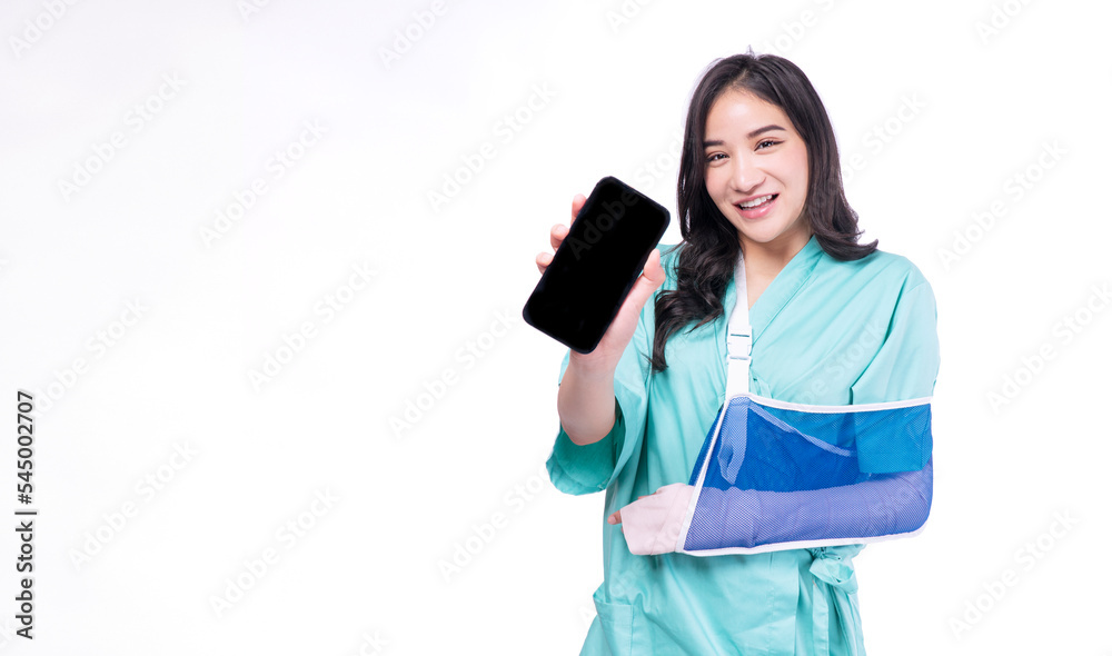 Injured asian woman painful accident broken hand soft splint arm showing blank mobile phone standing on white background. Smile young girl hold smartphone over isolated.Insurance accident health care. Injured asian woman painful accident broken hand soft splint arm showing blank mobile phone standing on white background. Smile young girl hold smartphone over isolated.Insurance accident health care.