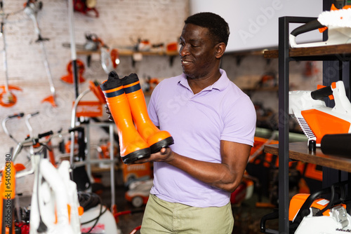 African-american man selecting new boots in gardening tools shop. © JackF