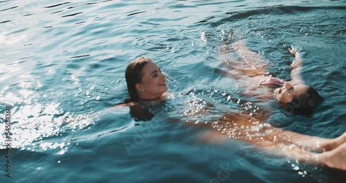 Two young women floating on top of the water in sunset