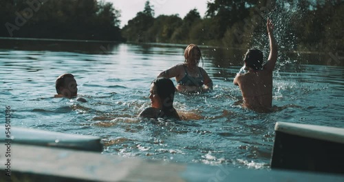 Small group of friends in a lake splashing water to eachother in the sunset photo
