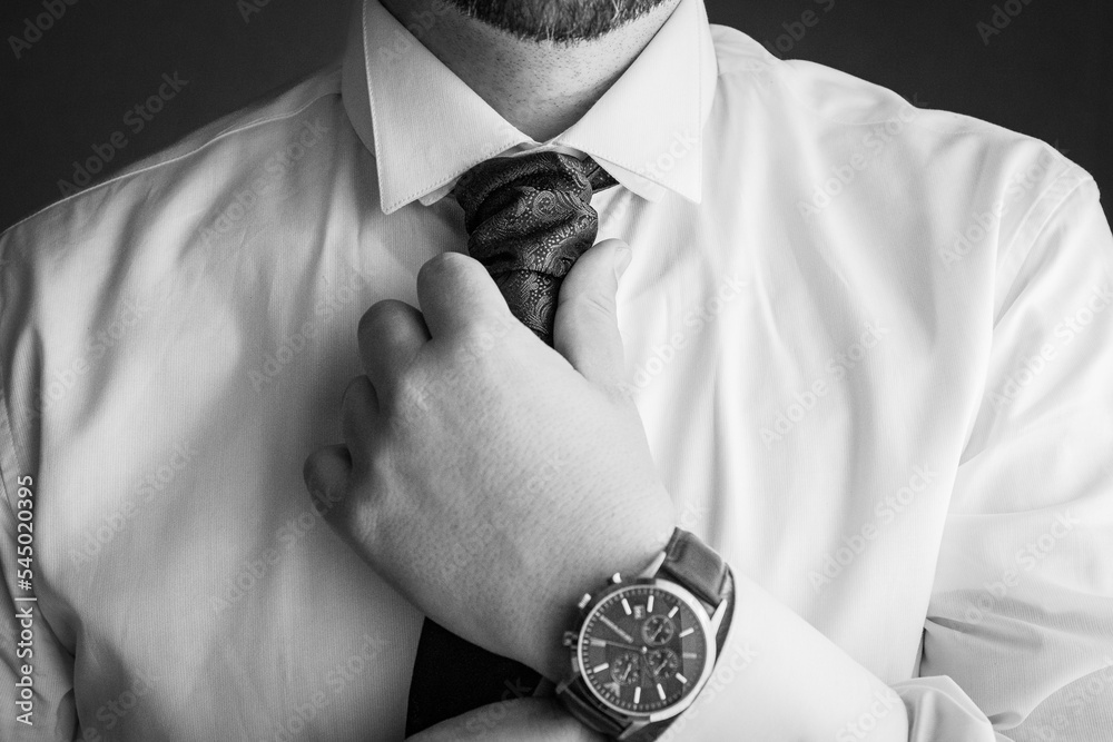 dettagli durante una cerimonia che ritrae lo sposo che si aggiusta la cravatta e mostra il dettaglio del collo orologio da polso del suo matrimonio in bianco e nero Stock Photo