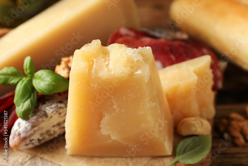 Delicious parmesan cheese, sausage and basil on wooden table, closeup