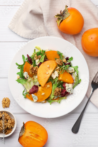Delicious persimmon salad and fork on white wooden table, flat lay