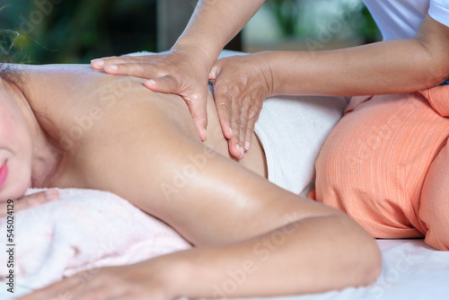 An elderly Asian woman receives a pain-relieving massage by a herbal therapist in a traditional Thai position.