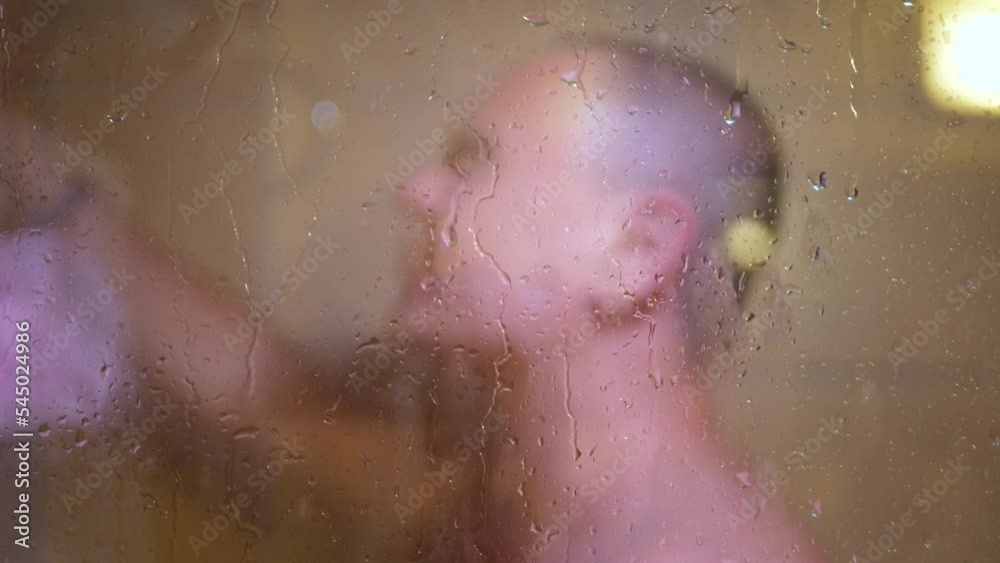 Unrecognizable man washing in bathroom. Cleaning body, remove stress and health care concept. Glass wall with water drops