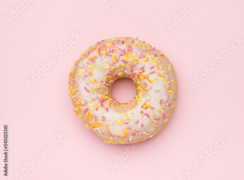 A light glazed donut sprinkled with sweet decorations on a pink background. The minimal concept of popular baking.