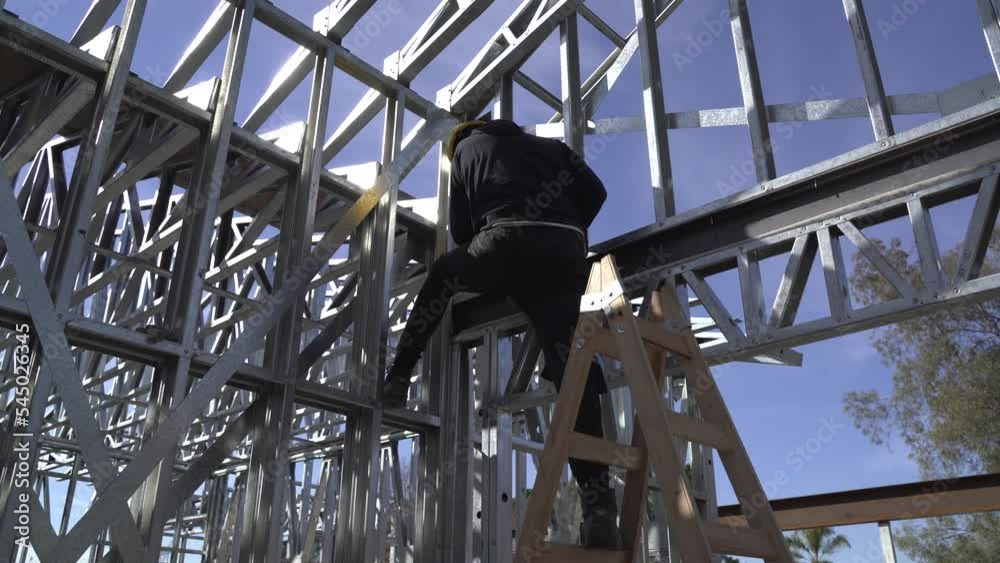 4K30 man standing on a ladder building a steel frame house