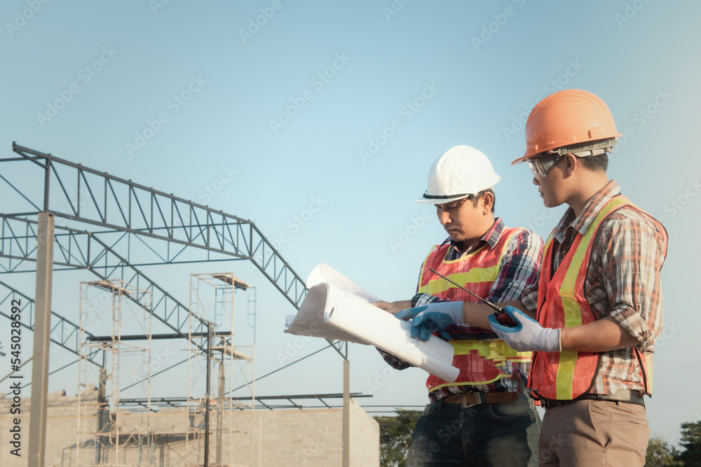 Structural engineer and worker working with blueprints discuss at the outdoors construction site.