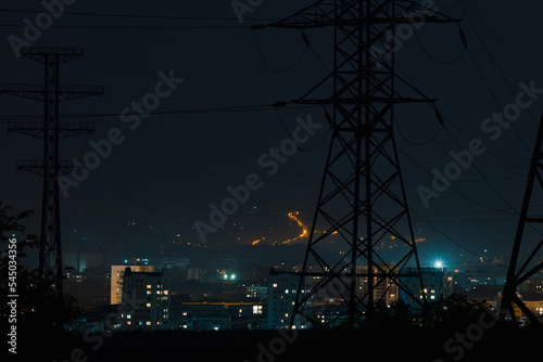 lights of a night city, buildings and houses of a residential area against the background of large high voltage poles, structures of power lines