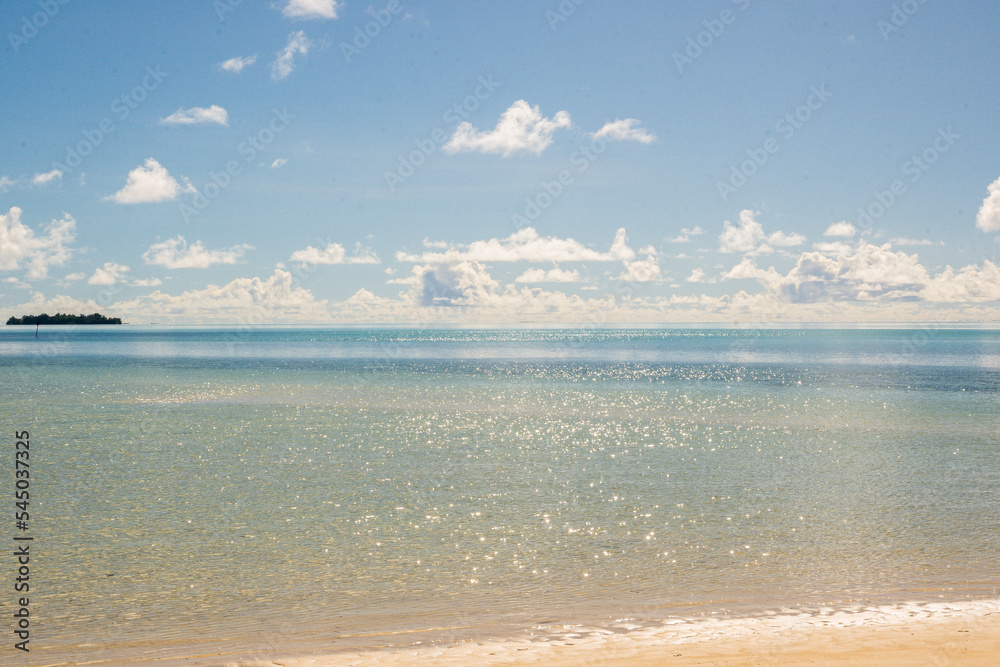 sea, beach and sky with clouds. The sea shining under the blue sky. The white line of the rock reef stretches all the way along the horizon.