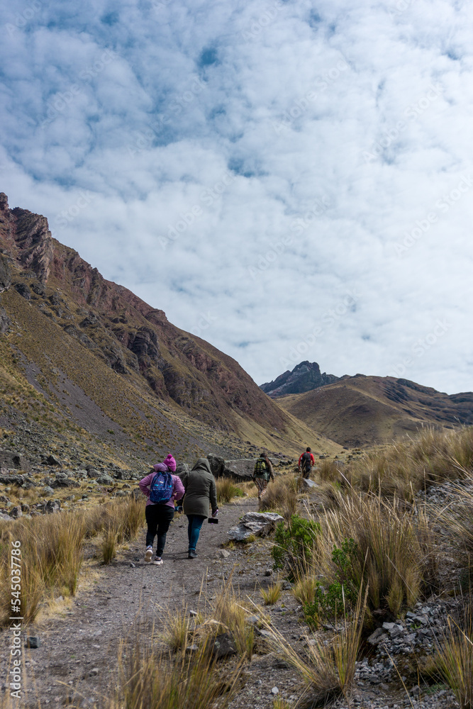 Cuatro personas caminado por un sendero hacia la montaña, y el cielo nublado, en los andes de PERÚ Sudamérica
