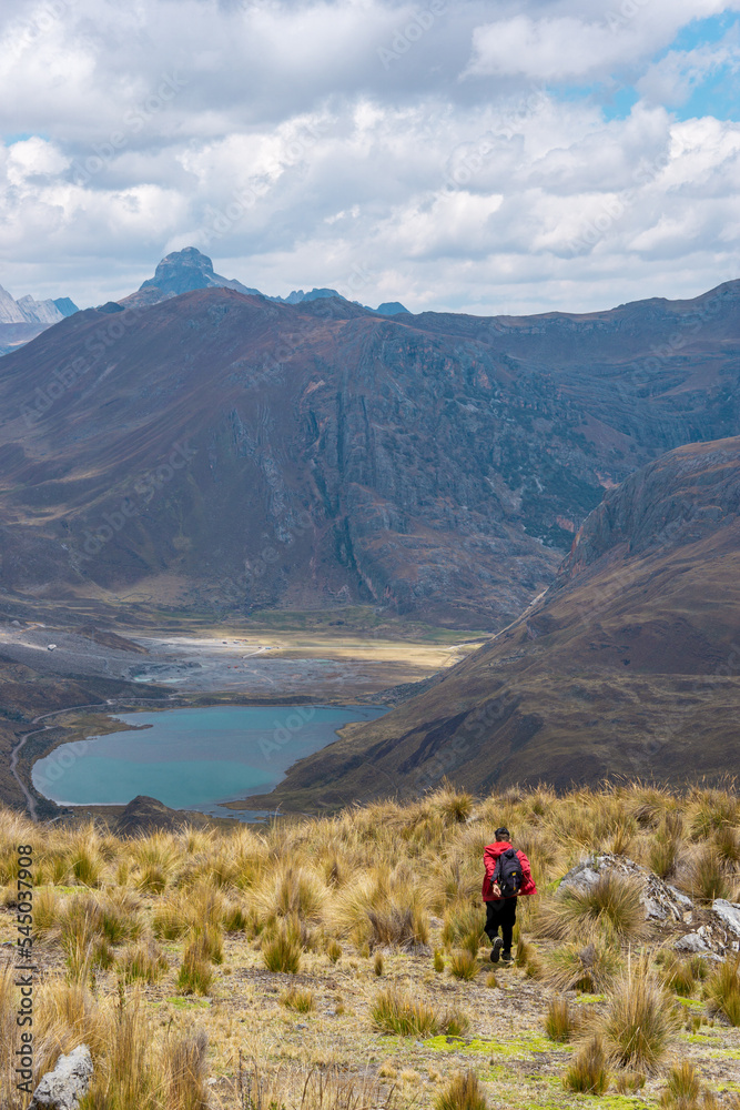 Hombre con mochila Caminado en una meseta o páramo, hacia una laguna y una montaña con el cielo nublado, en los Andes Perú Sudamérica 