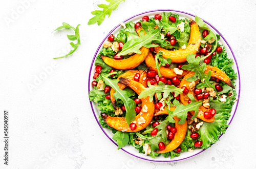 Autumn pumpkin salad with baked honey pumpkin slices, lettuce, arugula, pomegranate seeds and walnuts. Healthy vegan eating, comfort food. Top view
