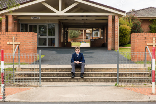 Boy sitting on steps at front of private catholic school smiling in uniform photo