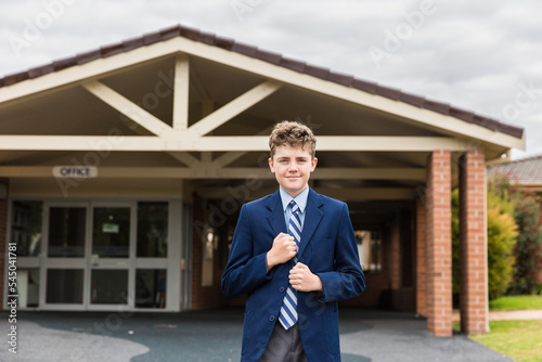 Child in uniform standing in front of school office holding blazer smiling photo