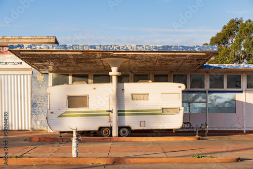 A large retro style caravan parked under the canopy of an abandoned service station photo