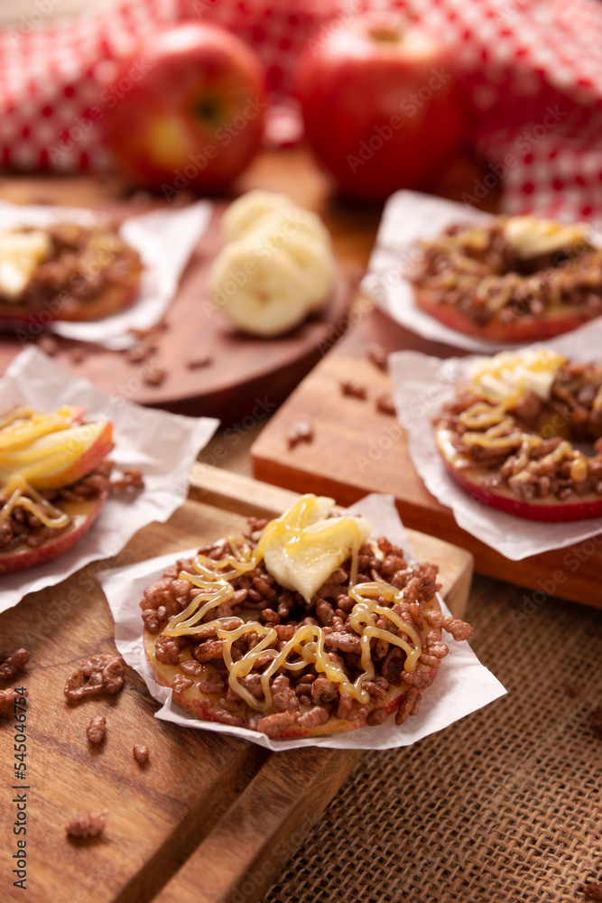 Creative party snack for holidays. Apple rounds with peanut butter, caramel and chocolate flavor puffed rice topping with banana slices. Funny appetizer for kids and adults. Creative party snack for holidays. Apple rounds with peanut butter, caramel and chocolate flavor puffed rice topping with banana slices. Funny appetizer for kids and adults.