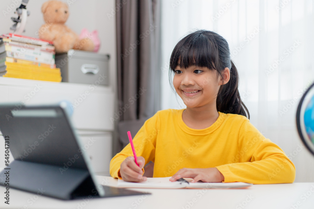 Asian schoolgirl doing her homework with digital tablet at home. Children use gadgets to study. Education and distance learning for kids. Homeschooling during quarantine. Stay at home Asian schoolgirl doing her homework with digital tablet at home. Children use gadgets to study. Education and distance learning for kids. Homeschooling during quarantine. Stay at home
