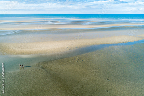 Aerial view of two fishermen walking over tidal sand flats towards deeper water. photo