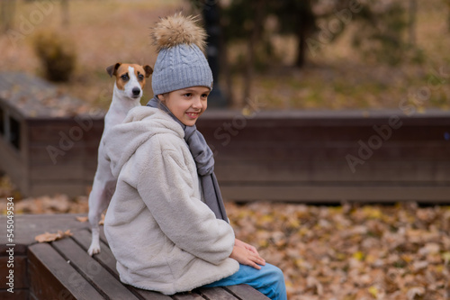 Caucasian girl sits on a bench with a dog Jack Russell Terrier for a walk in the autumn park. 