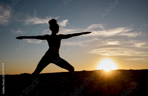 Silhouette, yoga and sunset with woman on rock for training, fitness and zen wellness. Spiritual, faith and health with pilates girl workout with warrior pose in nature for relax, peace and balance