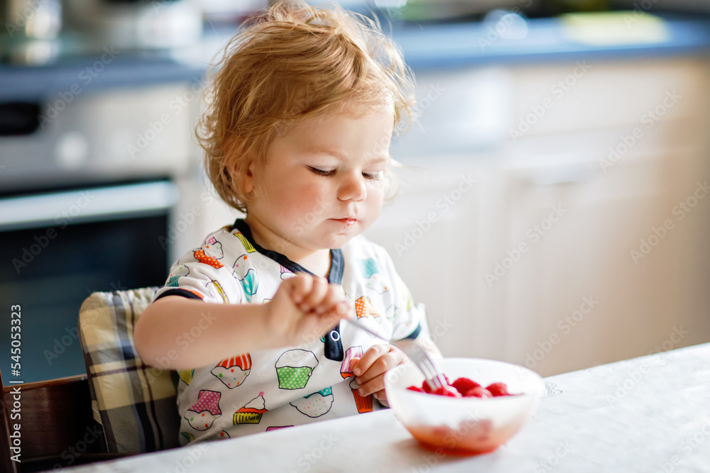 Adorable baby girl eating from spoon fresh healthy raspberries food, child, feeding and development concept. Cute toddler, daughter with spoon sitting in highchair and learning to eat by itself. Adorable baby girl eating from spoon fresh healthy raspberries food, child, feeding and development concept. Cute toddler, daughter with spoon sitting in highchair and learning to eat by itself.