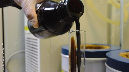 Black OIL sample being poured into TEST CYLINDER during LABORATORY testing for quality and contamination control.