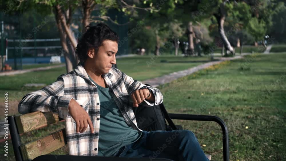 Disappointed lonely Latino guy waiting meeting checking time watch on bench at summer sunny park Disappointed lonely Latino guy waiting meeting checking time watch on bench at summer sunny park
