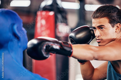 Fitness, boxing and man at gym for exercise, training and workout with a dummy for fast, speed and agile punch for sports match or competition. Focus, face and boxing gloves on athlete boxer to fight © Beaunitta V W/peopleimages.com